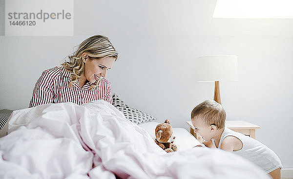 Lächelnde Mutter spielt mit Kleinkind-Sohn zu Hause im Bett