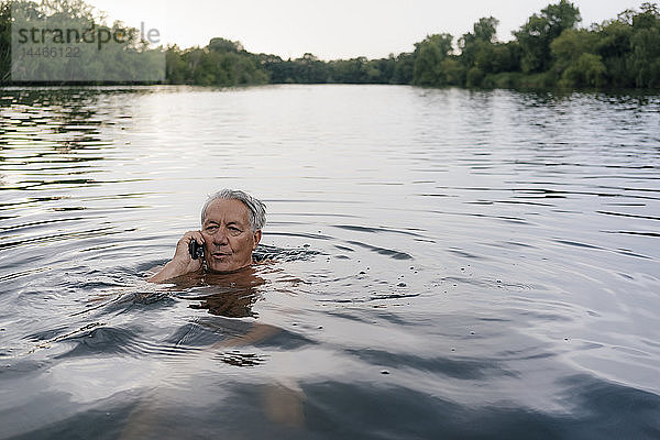 Älterer Mann telefoniert mit seinem Handy in einem See