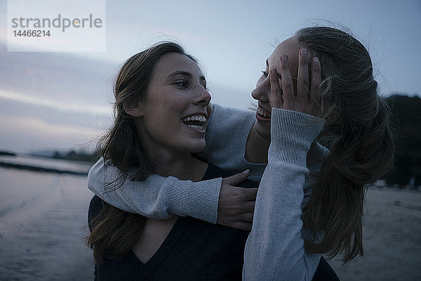 Deutschland  Hamburg  zwei fröhliche Teenager-Mädchen  die sich abends am Strand am Elbufer umarmen