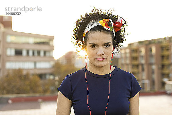 Porträt einer jungen Frau mit Haarreif und Kopfhörer in der Stadt bei Sonnenuntergang