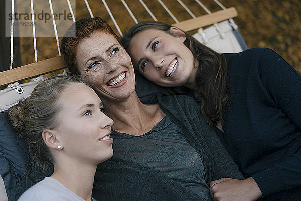 Glückliche Mutter mit zwei Mädchen im Teenageralter  die im Herbst in der Hängematte im Garten liegen