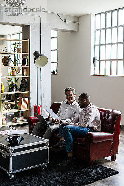Zwei Geschäftsleute  die einen Laptop benutzen und Dokumente auf dem Sofa im Loft-Büro besprechen