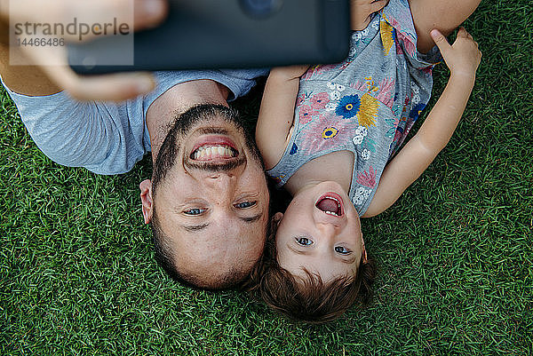Glückliche Vater und Tochter beim Selfie mit Handy auf grünem Gras