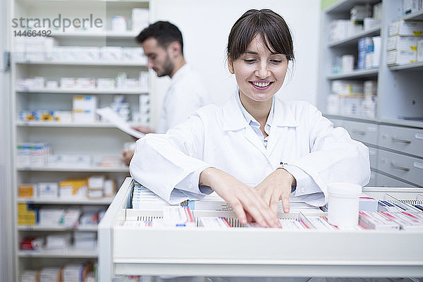 Lächelnder Apotheker sucht Medizin am Kabinett in der Apotheke