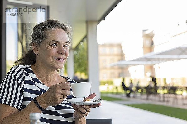 Porträt einer lächelnden reifen Frau  die auf der Terrasse eine Tasse Kaffee trinkt