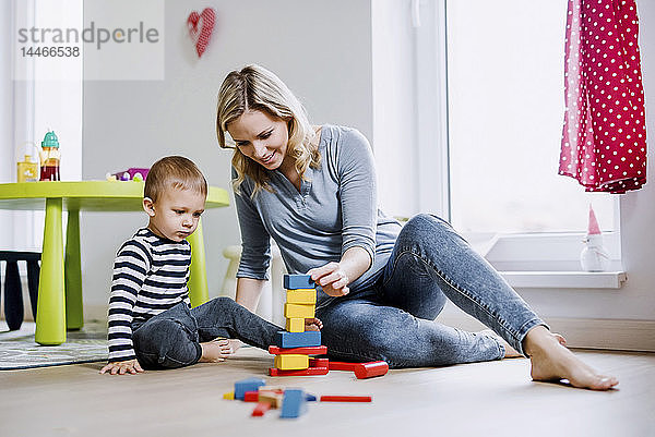 Lächelnde Mutter und Kleinkind spielen zu Hause mit Bausteinen