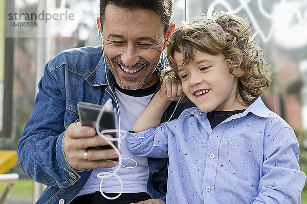 Glücklicher Vater und Sohn teilen sich Handy und Kopfhörer