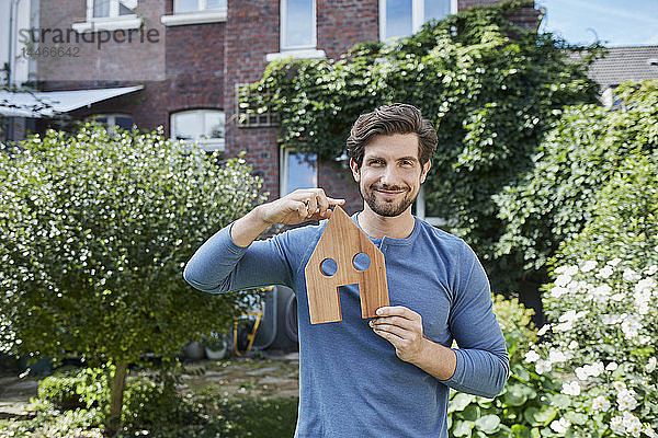Porträt eines lächelnden Mannes vor dem Modell seines Wohnhauses