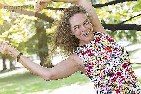 Porträt einer glücklichen  reifen Frau in einem Top mit Blumenmuster  die in einem Park tanzt
