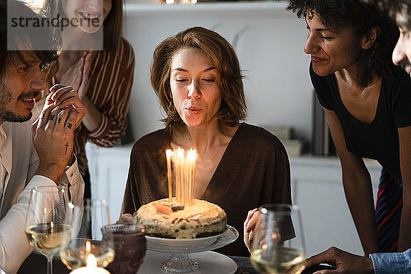 Freunde feiern den Geburtstag einer jungen Frau  blasen Geburtstagskerzen aus