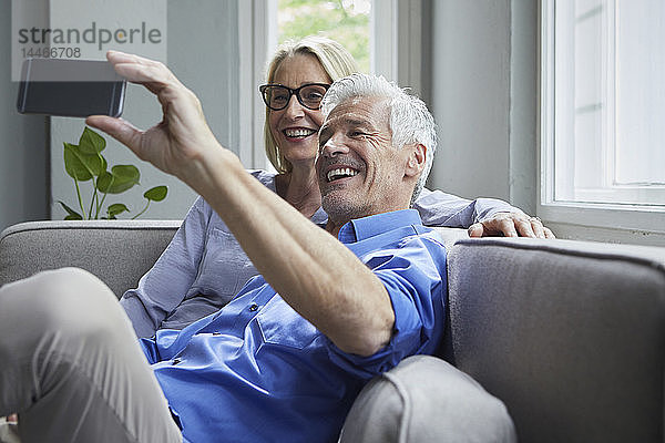 Glückliches reifes Paar  das zu Hause auf der Couch sitzt und sich ein Selfie