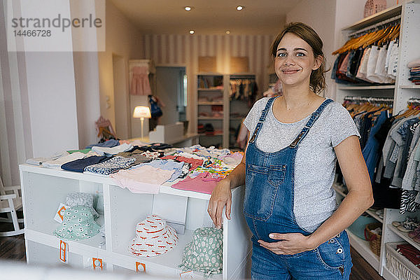 Porträt einer lächelnden schwangeren Frau in einer Boutique für Babykleidung