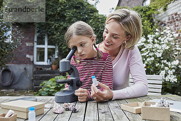 Mutter und Tochter unter dem Mikroskop zusammen am Gartentisch