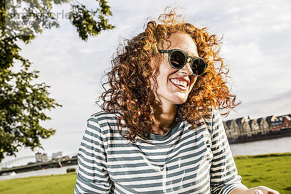 Deutschland  Köln  Porträt einer lachenden rothaarigen jungen Frau mit Sonnenbrille