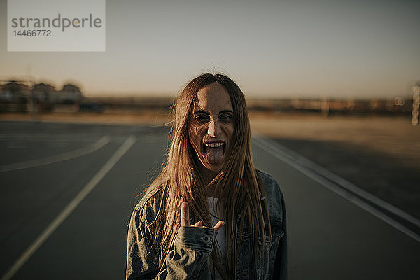 Porträt einer jungen Frau im Freien mit herausgestreckter Zunge