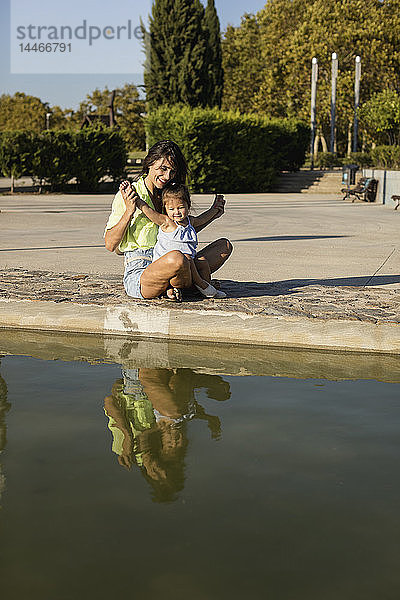 Glückliche Mutter mit Tochter an einem Pool in einem Park