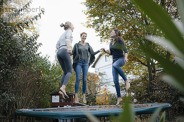 Glückliche Mutter mit zwei Mädchen im Teenageralter  die im Herbst im Garten auf dem Trampolin springen