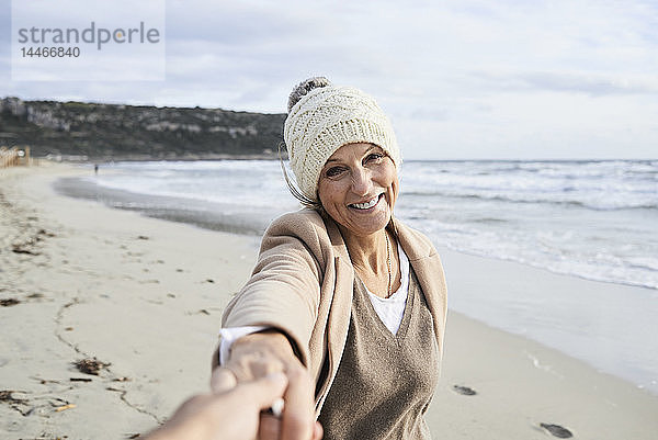 Spanien  Menorca  Porträt einer glücklichen älteren Frau  die im Winter am Strand die Hand hält