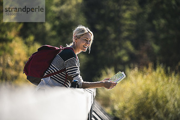 Österreich  Alpen  glückliche Frau auf einer Wanderung mit Karte auf einer Brücke