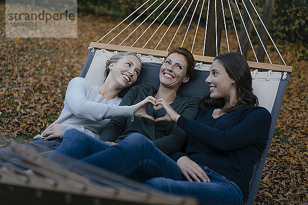 Glückliche Mutter mit zwei Mädchen im Teenageralter  die im Herbst in der Hängematte im Garten liegen