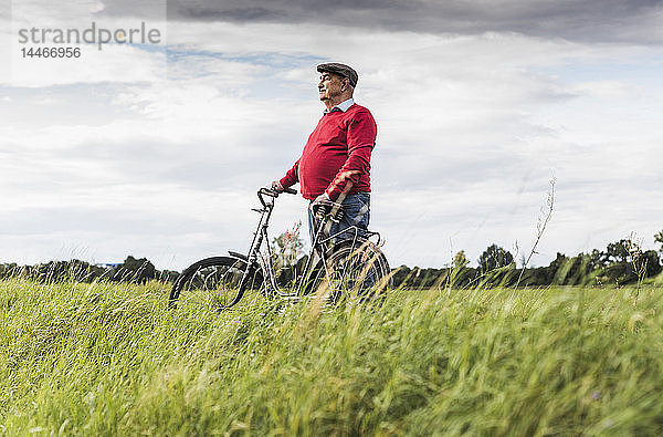 Älterer Mann mit Fahrrad in ländlicher Landschaft