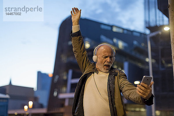 Spanien  Barcelona  aufgeregter älterer Mann mit Kopfhörern und Handy in der Stadt in der Abenddämmerung