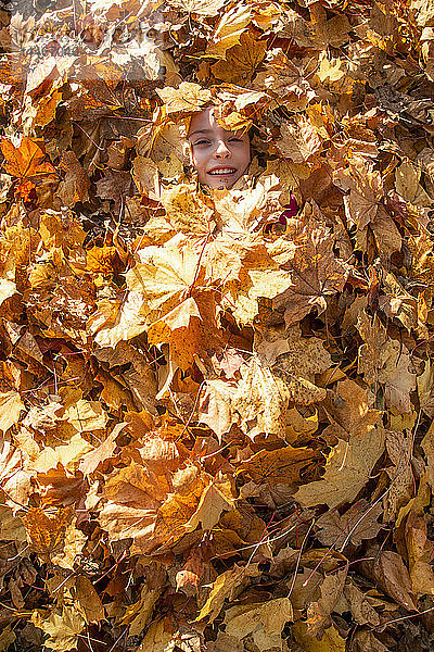 Lächelndes Mädchen mit Herbstlaub bedeckt
