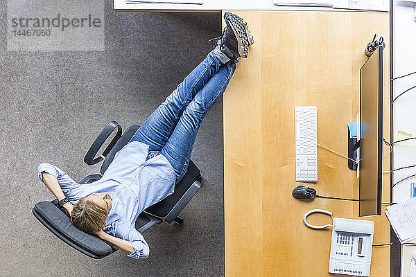 Draufsicht einer Frau  die sich auf einem Stuhl am Schreibtisch im Büro entspannt
