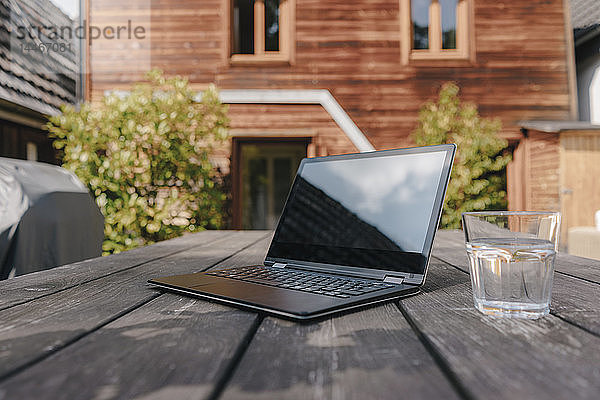 Laptop und Wasserglas auf dem Tisch auf der Terrasse