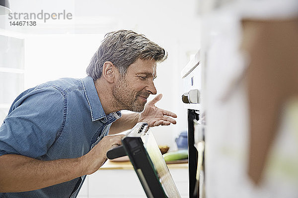 Ein erwachsener Mann in seiner Küche riecht das Essen im Ofen