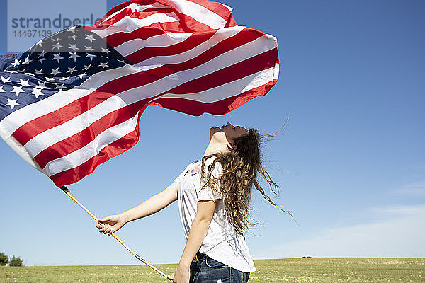 Glückliches Mädchen mit amerikanischer Flagge auf Feld in entlegener Landschaft