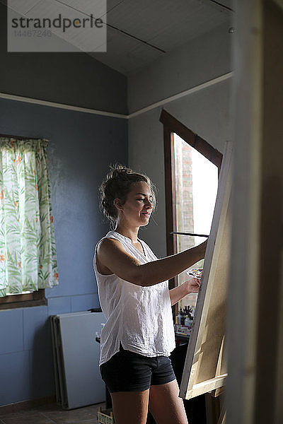 Lächelnde junge Frau malt in ihrem Atelier