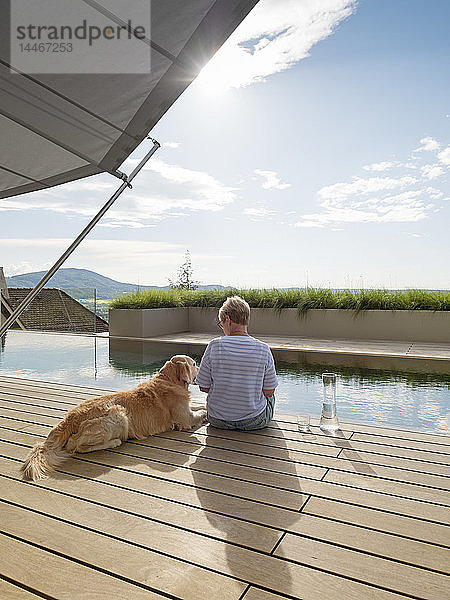 Ältere Frau sitzt mit Hund am Poolrand