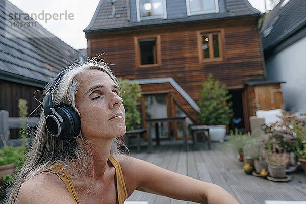 Porträt einer reifen Frau  die auf der Terrasse mit Kopfhörern Musik hört