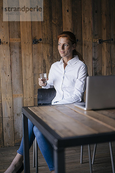 Geschäftsfrau sitzt am Schreibtisch mit einem Glas Wasser und einem Laptop