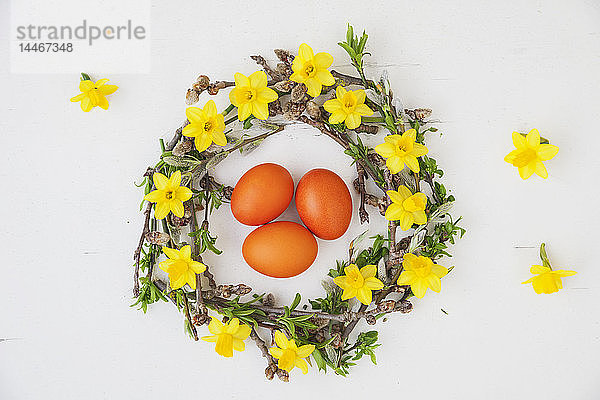 Selbstgemachter Osterkranz und orange gefärbte Eier auf weißem Grund