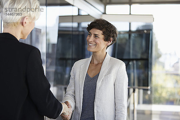 Zwei Geschäftsfrauen schütteln sich im Amt die Hand