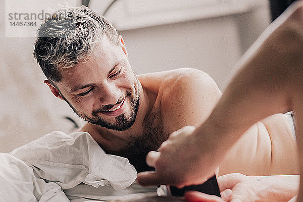 Porträt eines lächelnden schwulen Mannes mit seiner Partnerin im Bett