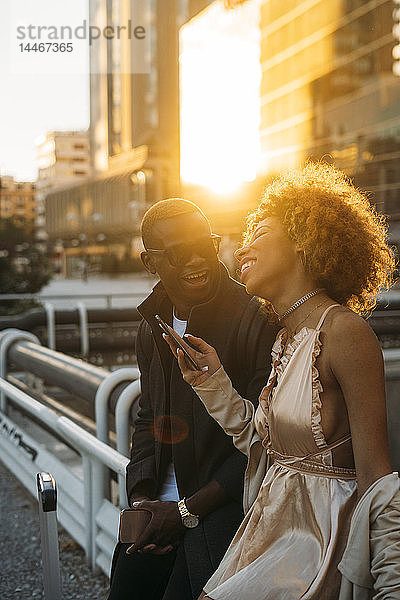 Glückliches Paar mit Mobiltelefonen in der Stadt bei Sonnenuntergang