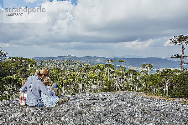 Chile  Puren  Nahuelbuta-Nationalpark  Frau sitzt mit Söhnen auf einem Felsblock und schaut auf den Araukarien-Wald