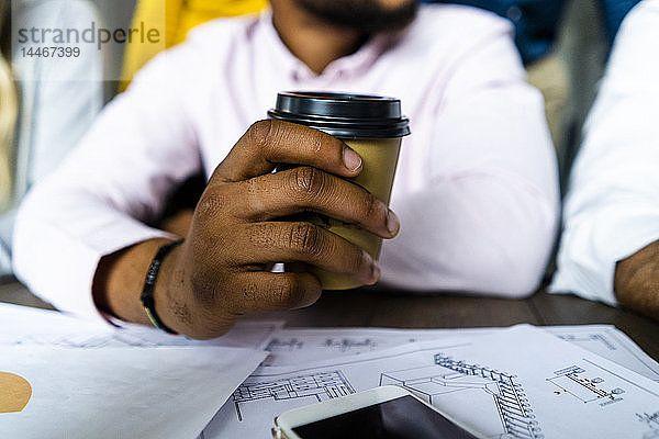 Nahaufnahme eines Geschäftsmannes mit einer Einweg-Kaffeetasse während einer Sitzung im Amt
