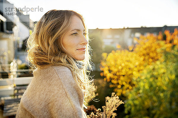 Blonde reife Frau genießt sonnigen Herbsttag auf dem Balkon
