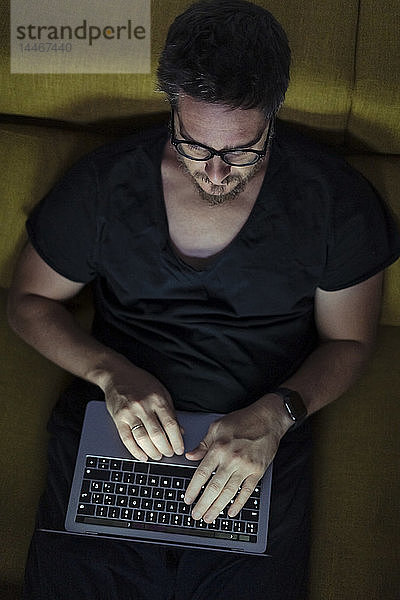 Mann sitzt nachts mit Laptop auf dem Sofa