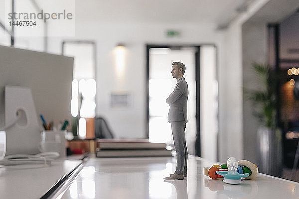 Geschäftsmann-Figur auf Schreibtisch stehend mit Schnuller und Spielzeug