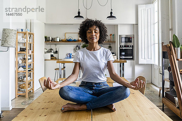 Lächelnde Frau mit geschlossenen Augen in Yoga-Pose auf Tisch zu Hause