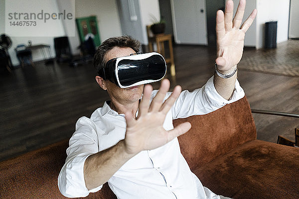 Reifer Mann mit VR-Brille sitzt auf einer Couch auf einem Dachboden