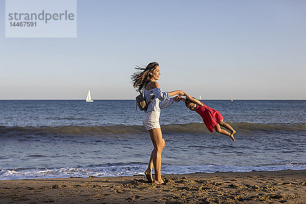 Mutter und Tochter amüsieren sich am Strand und tun so  als würden sie fliegen