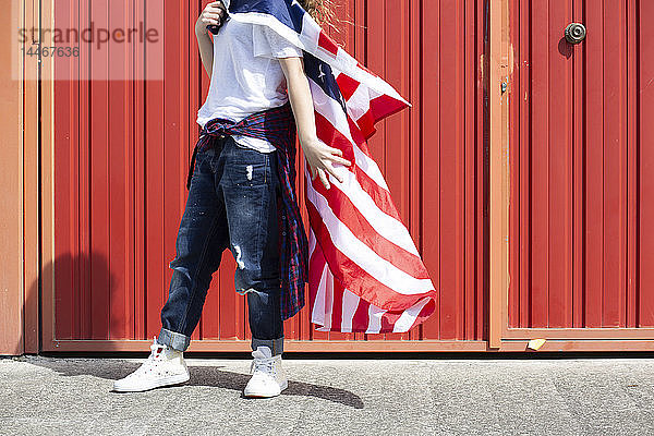 An roter Wand stehendes Mädchen mit amerikanischer Flagge