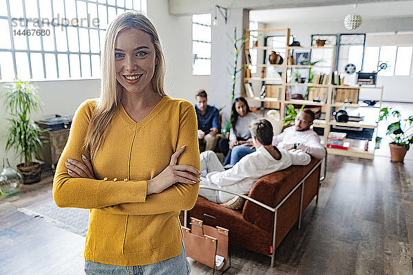 Porträt einer lächelnden jungen Geschäftsfrau mit Mitarbeitern im Hintergrund in einem Loft-Büro