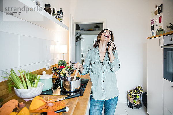 Lachende Frau spricht am Telefon  während sie Kürbissuppe zubereitet